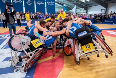 Gruppe Basketballer in Rollstühlen umarmen sich, bilden so einen großen Kreis.