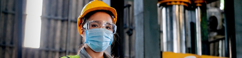 Frau in einer Werkshalle mit Helm, Maske und Warnweste