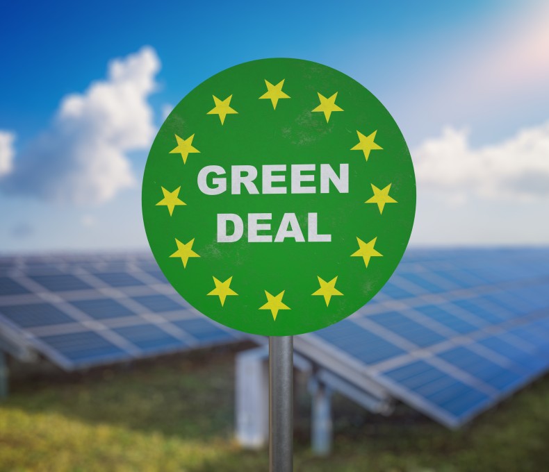 Auf einem grünen runden Schild steht: Green Deal; im Hintergrund sind Solarpanele zu sehen Auf einem grünen runden Schild steht: Green Deal; im Hintergrund sind Solarpanele zu sehen