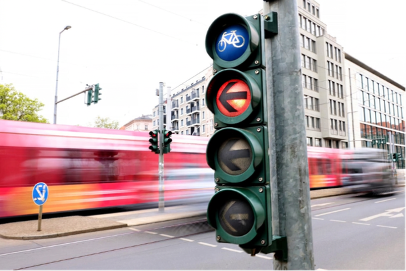 Ampel mit Fahrradsymbol zeigt Rot, Straßenbahn fährt im Hintergrund vorbei.
