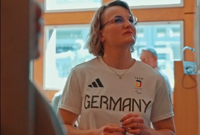 Anna-Lena Forster, Monoski-Fahrerin mittleren Alters, halblange, leicht wellige Haare im Gespräch mit anderen, die allerdings durch eine verdeckende Tür nicht vollständig zu sehen sind.